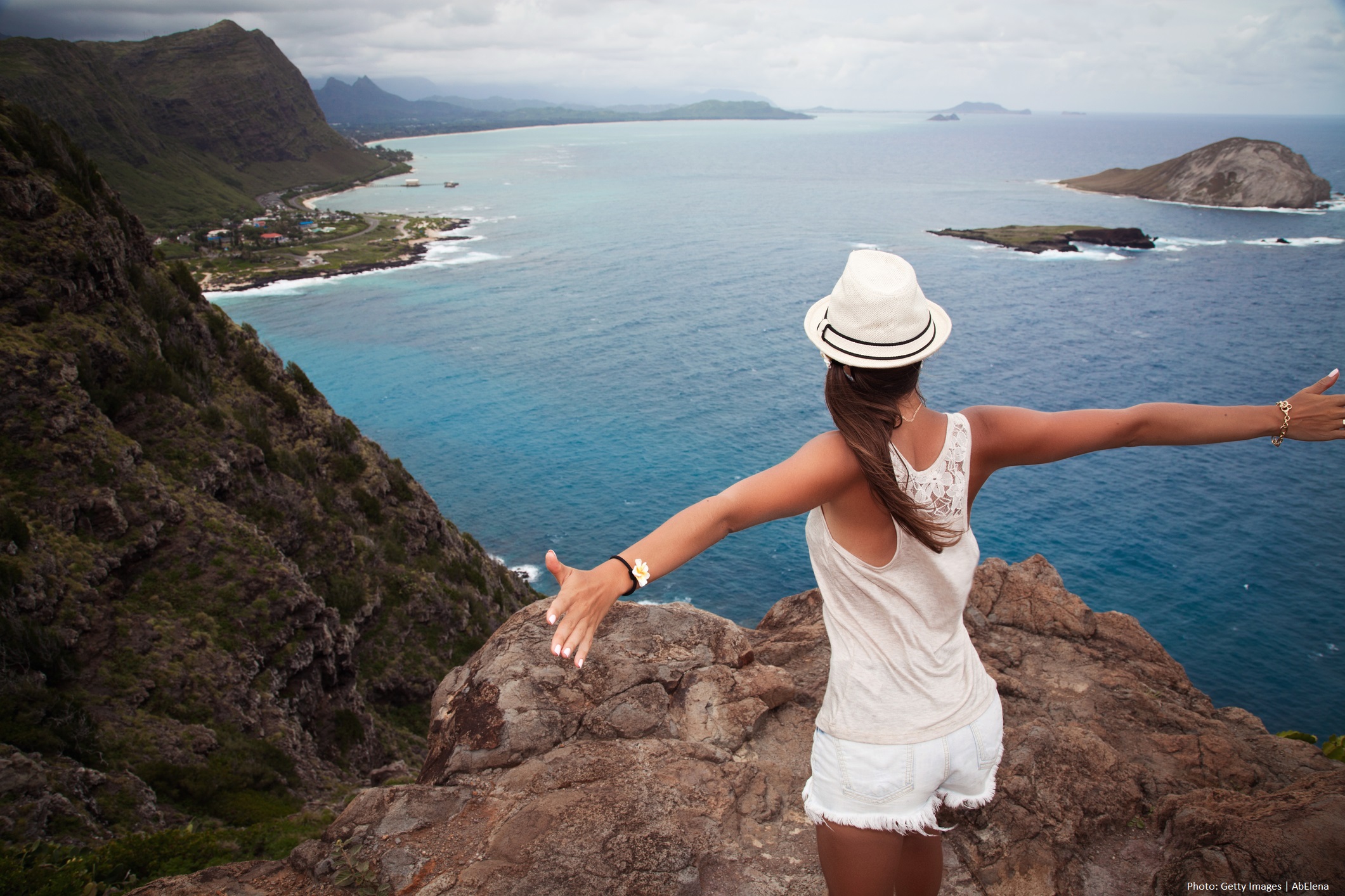 Young happy woman standing on a rock with raised hands and looking at view of beautiful Hawaiian landscape nature. Vacation travel.